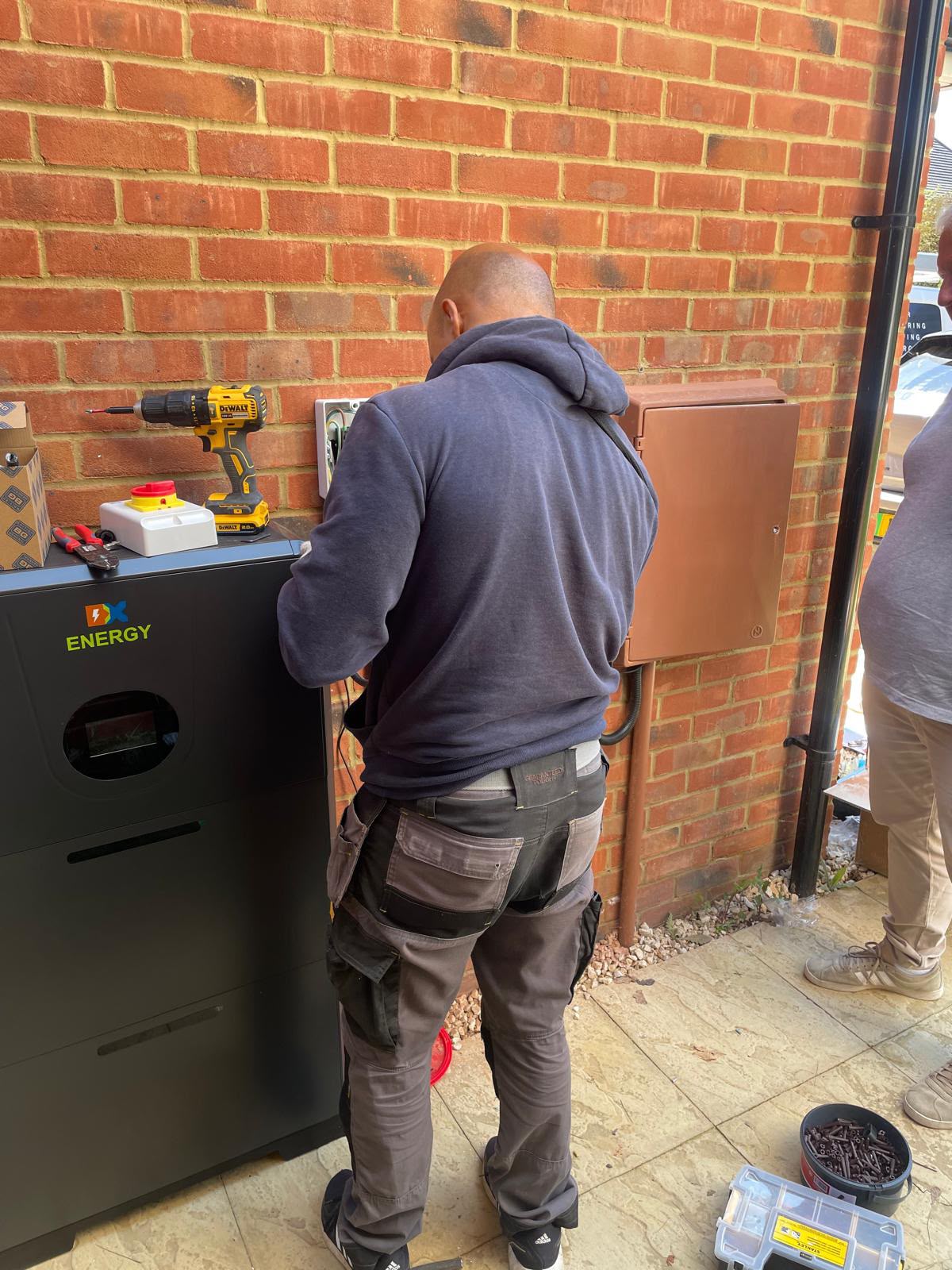 An installer working on the battery connections beside an exterior brick wall